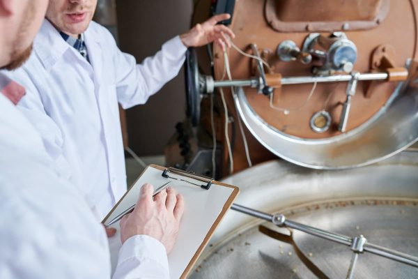 High angle closeup of two unrecognizable  workers wearing lab coats holding clipboard and discussing coffee processing,  copy space